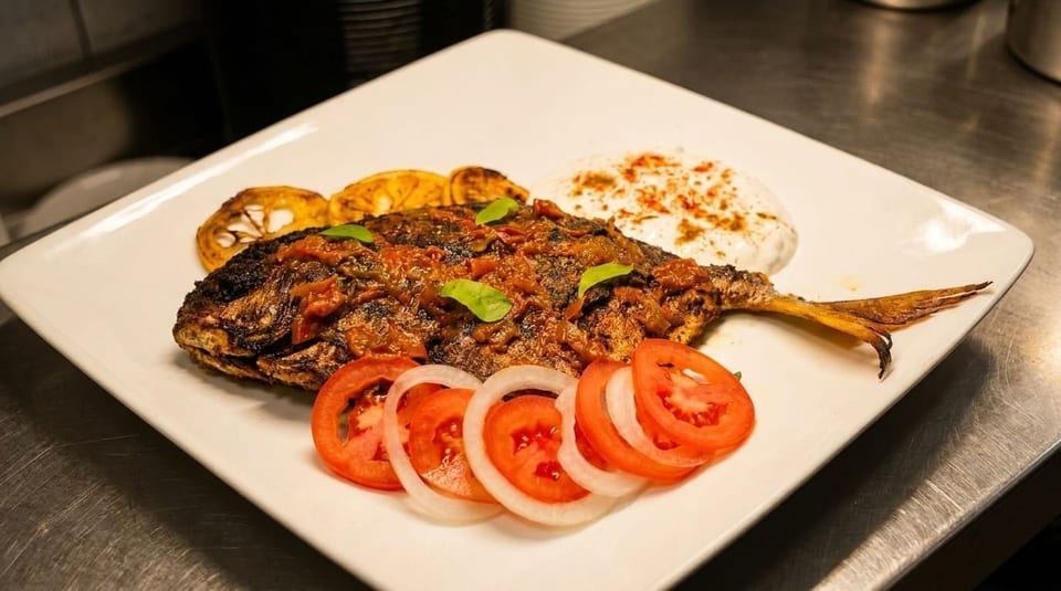 Whole grilled fish topped with tomato sauce, served with lemon, yogurt, and sliced tomatoes and onions.