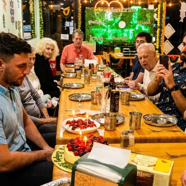 A group of people celebrating a birthday with cake and desserts at a restaurant table.