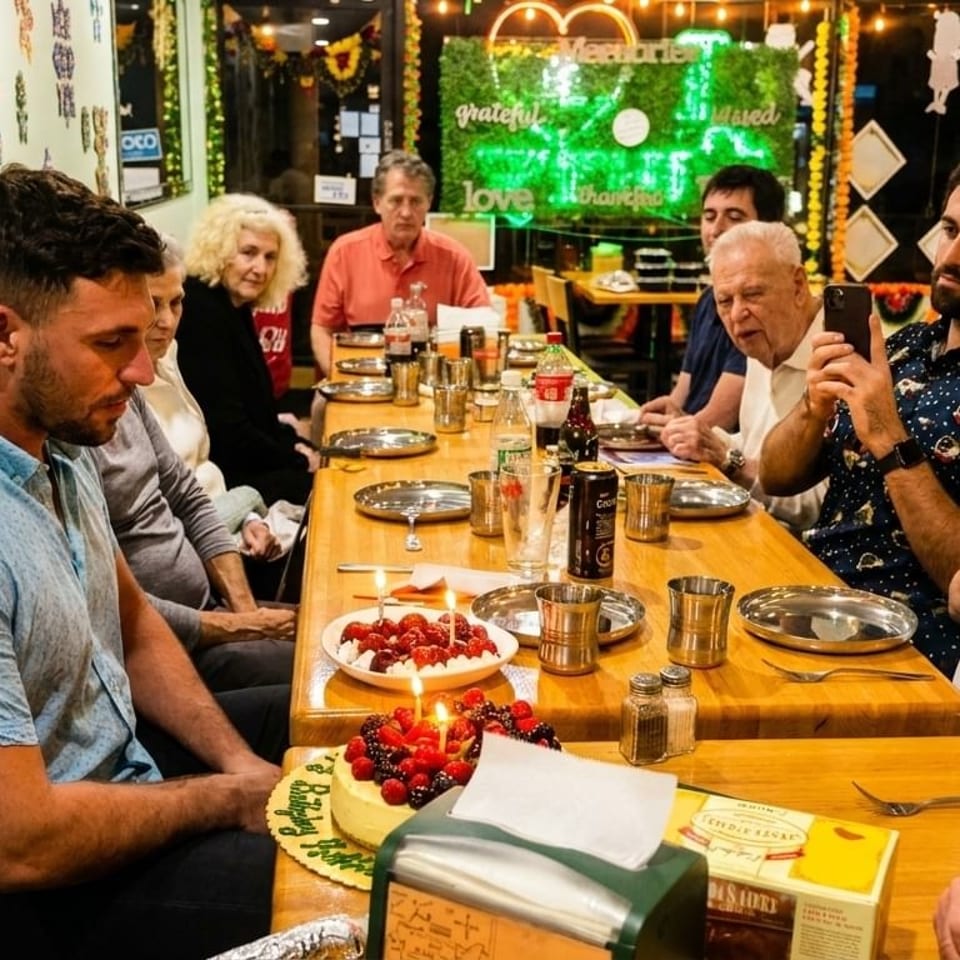 A group of people celebrating a birthday with cake and desserts at a restaurant table.