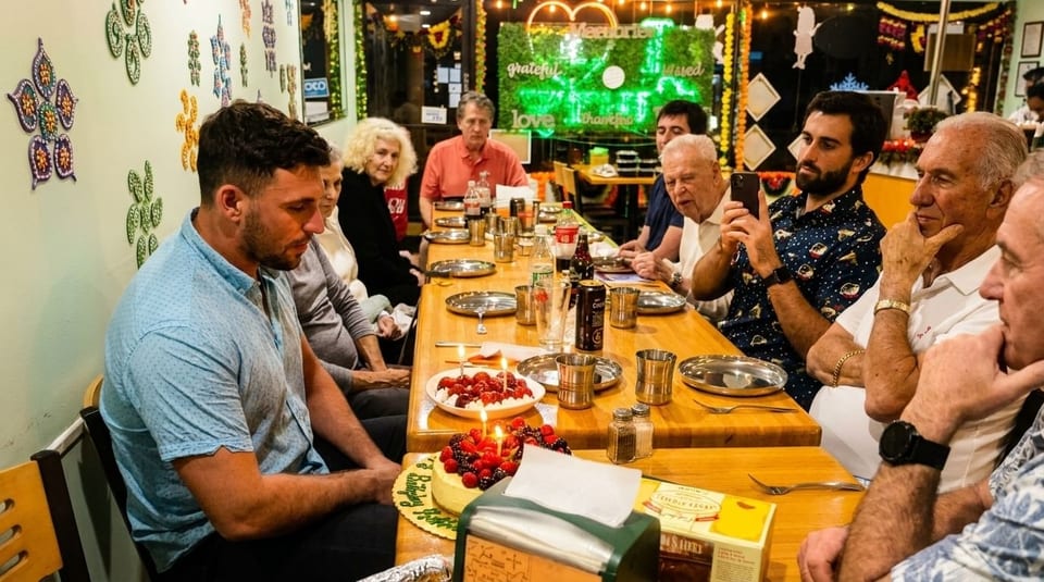 A group of people celebrating a birthday with cake and desserts at a restaurant table.