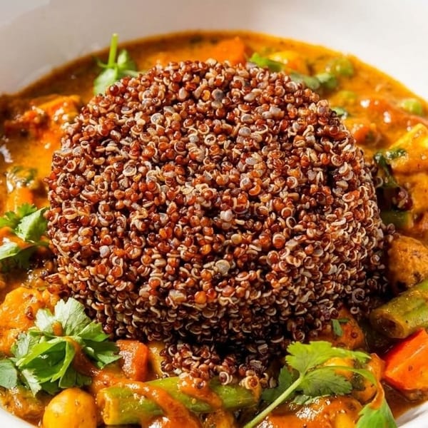 A white bowl filled with a vibrant curry, topped with a mound of red quinoa and fresh cilantro.