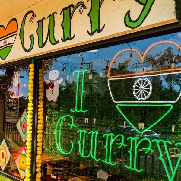 The exterior of I Curry restaurant with a neon sign and Indian flag heart in the window.